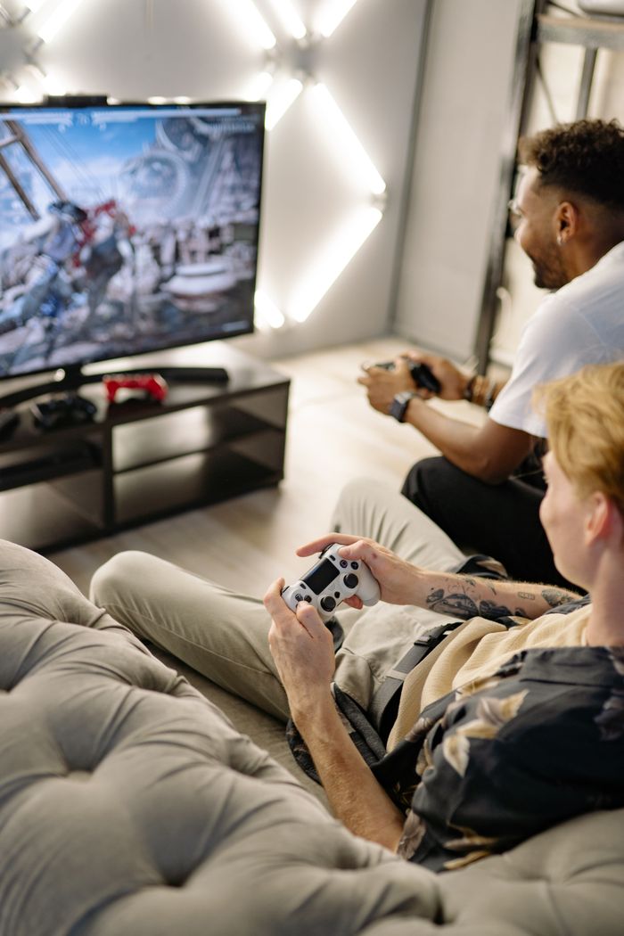 Mastering the First Impression: Your intriguing post title goes here Two friends playing video games at home, immersed in a gaming session with controllers and a big screen.